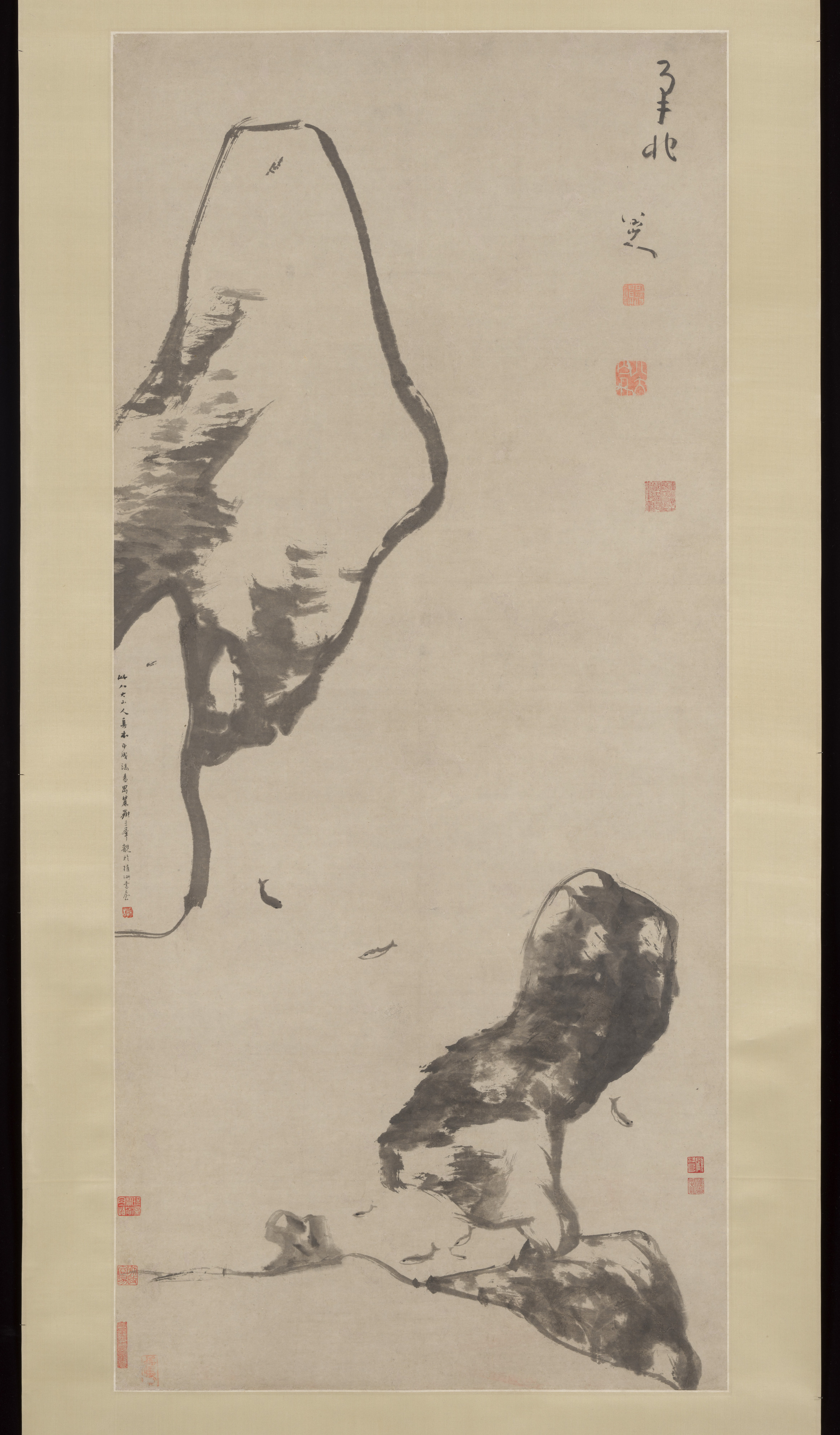 Bada Shanren’s ink hanging scroll with seven small fish swimming through blank paper beneath two large dark rocks.